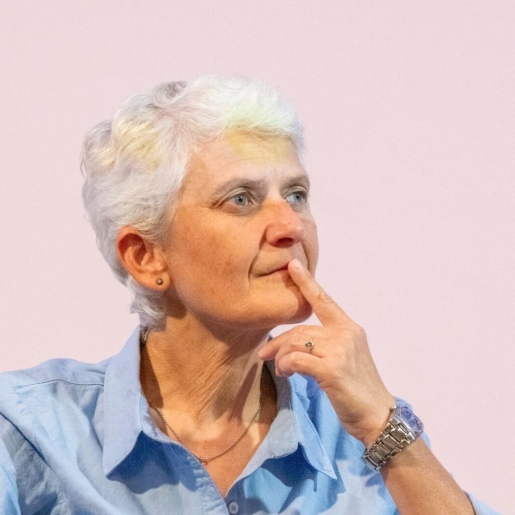 Primo piano di Marilena Grassadonia, referente diritti LGBT+ di Roma Capitale, con capelli corti bianchi e camicia azzurra, in atteggiamento pensieroso durante il festival Rainbook.